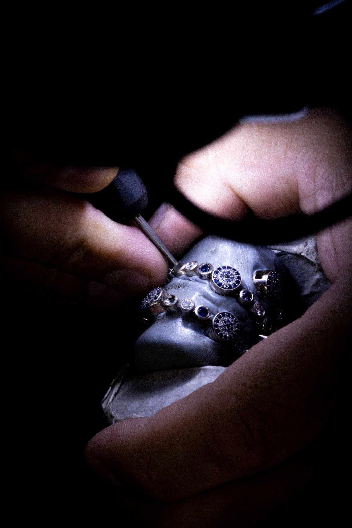 Goldschmied bei präziser Handarbeit an Ringen mit blauen Edelsteinen – Feinstbearbeitung und Finishing bei Precious Metal Casting AG (PMC).